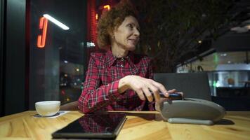 Female mature customer holding phone near nfc terminal make contactless mobile payment on coffeeshop counter, senior woman client pay in cafe with cellphone via pos machine. POS terminal. video
