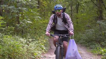 Athlete cycling riding through forest with garbage bag on the handlebars, cleaning up garbage and plastic during a bicycle trip in the forest. Ecology theme, pollution, rubbish and plastic discarded. video