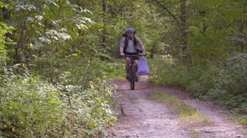 Athlete cycling riding through forest with garbage bag on the handlebars, cleaning up garbage and plastic during a bicycle trip in the forest. Ecology theme, pollution, rubbish and plastic discarded. video