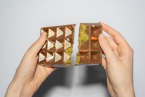 Trend Dubai chocolate with pistachio, tahini and kadaif broken in woman's hands. Confectionery handmade sweets, chocolatier photo