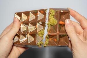Close up of famous Dubai chocolate with pistachio, tahini and kadaif broken in woman's hands. Confectionery handmade sweets, chocolatier photo
