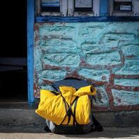 A yellow backpack rests quietly near a blue weathered wall. Concept of travel, exploration, and the essence of adventure. photo