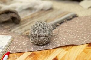 Rustic yarn ball on patterned fabric with wooden spools on table photo