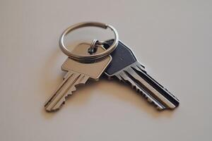 Two metal keys on key ring resting on white surface photo