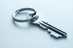 Single key with metal key ring resting on white surface photo