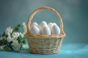 White eggs resting in a wicker basket on a teal tablecloth with white flowers photo