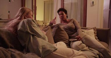 Multiracial women sitting on sofa in evening and having conversation video