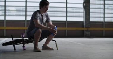 Tired male rider sitting on BMX and resting after practicing stunts video