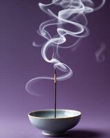 Incense stick smoking in bowl on purple background creating swirls of white smoke photo