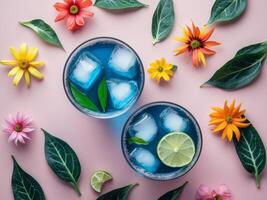 Refreshing butterfly pea tea with ice and lime surrounded by vibrant flowers and leaves on a pink background top view flat lay composition photo