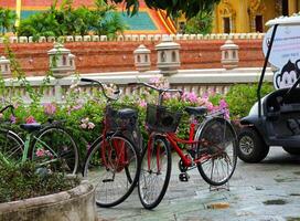 Bangkok, Thailand on 23 July 2023. Red and Green Bikes Resting in a Temple Garden on a Rainy Day photo