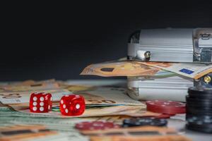 Close-up of two red dice on a table surrounded by euro bills, casino chips, and a metal case photo