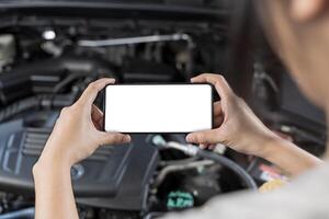 Close-up of woman's hands holding smartphone with empty space on screen for your text, background of car engine. photo