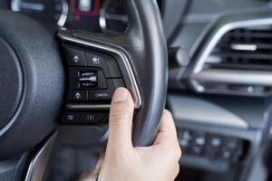 Woman's hand presses the button on the steering wheel of the car close-up. Multi function buttons photo