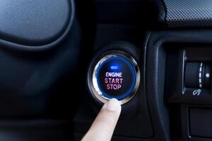 The driver palm as it presses the electric car engine start stop button with a blue light illuminated photo