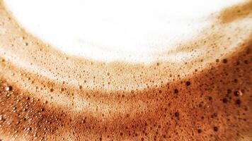 High-angle full-frame shot of coffee and milk swirling together, featuring frothy foam bubbles and creating a captivating abstract pattern. photo