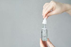 Caucasian female hands holding dropper and glass bottle against gray background for skincare or essential oils. photo