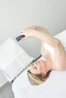 Caucasian young female using smartphone while lying on spa table in relaxing environment. photo
