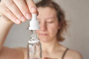 Caucasian female adult using skincare serum with dropper for facial routine at home. photo