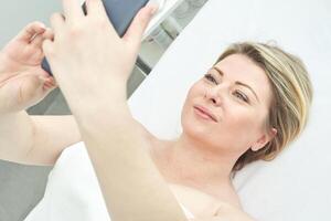 Caucasian mature woman relaxing and taking selfie in spa setting with smartphone. photo