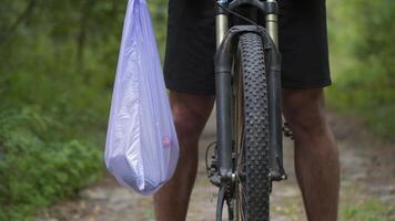 Man riding bicycle through forest, picking up trash. Trendy sports plogging programs to help save nature. Pollution of environment. Ecological issue. Plastic ban awareness, national cleanup days idea. video