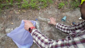 Safe planet, man hiker with backpack collects garbage in plastic trash bag in forest for clean planet, environment and ecology while walking in nature. Green volunteering. Man hand picking up garbage. video
