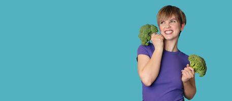 Broccoli in the hand of a slender smiling woman on a blue background. A panoramic banner with a place for your text. healthy lifestyle. photo