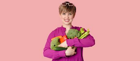 A studio shot of a young woman holding a lot of fresh vegetables in her hands. The concept of healthy eating. Vegetarianism. A panoramic banner with a copy of the space. photo