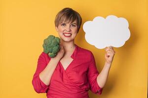 A studio shot of a young smiling woman holding fresh broccoli and a blank letterhead. The concept of healthy eating. photo