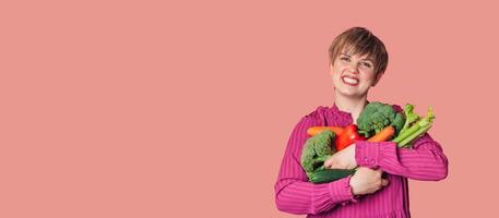 Studio shot, a young Caucasian woman holding a lot of fresh vegetables in her hands. The concept of healthy eating. Vegetarianism. A panoramic banner with a copy of the space. photo