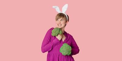 Studio shot of a young Caucasian woman in bunny ears holding organic and fresh broccoli in her hands. healthy eating.A panoramic banner with a copy of space. photo