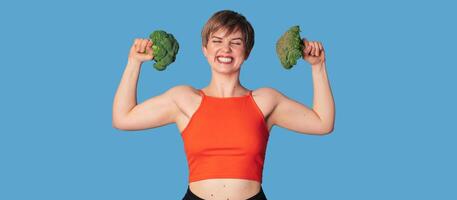 A smiling Caucasian girl with fresh broccoli in her hands as dumbbells. Panoramic banner, free space. photo