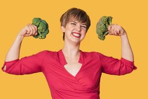 Broccoli in the hand of a slender smiling woman on a yellow background. healthy lifestyle. photo