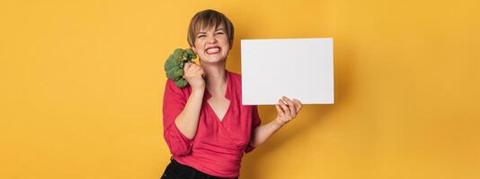 A studio shot of a young smiling woman holding fresh broccoli and a blank letterhead. The concept of healthy eating. A place for your text. Panoramic banner. photo