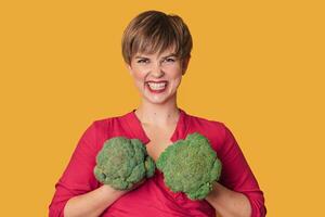 Broccoli in the hand of a slender smiling woman on a yellow background. healthy lifestyle. photo
