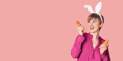 Smiling slender Caucasian girl in bunny ears with fresh carrots in her hands. Panoramic banner, free space. Organic vegetables. photo