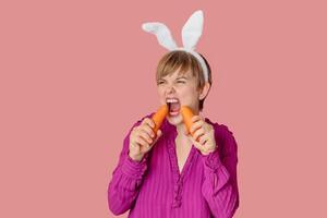 Smiling slender Caucasian girl in bunny ears with fresh carrots in her hands. Organic vegetables. photo