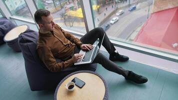 man working with laptop while sitting on armchair near panoramic window video