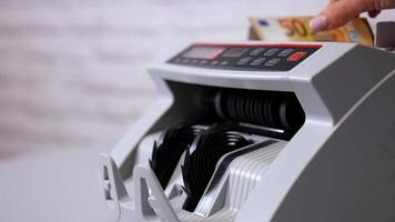 Female teller putting money into currency counting machine at cash department, close up video