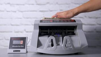 Money counting equipment for paper money calculation. US Dollar bills. Woman putting money into counting machine at table indoors, close up. video