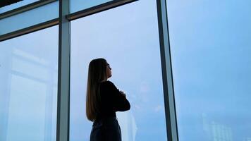 Pensive businesswoman dressed in formal apparel standing near panoramic window in enterprise company video