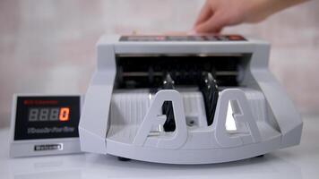Woman putting money into counting machine at table indoors, close up. video