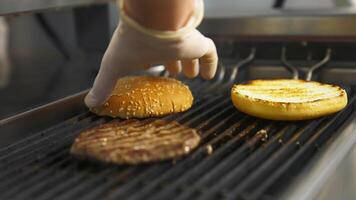 Side view of the delicious burger cutlet and two buns flipped on the grill with hand in latex gloves. Selective focus. video