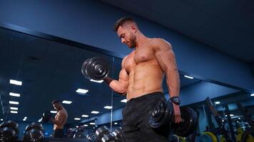 Handsome bodybuilder trains with dumbbells in modern gym. Slow motion. video