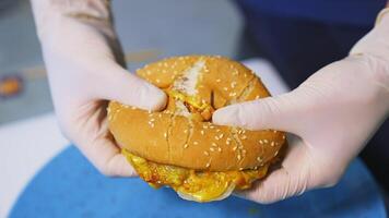Fast food. Macro view of breaking burger. Hands in white latex gloves break burger in a half, showing tasty cheese and cutlet. Closeup. video