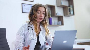 Coronavirus, medical staff member talks about healthcare standards using modern webcam technology on laptop. Beautiful medic woman in headphones with microphone. video