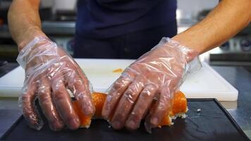 Chef in restaurant prepares sushi rolls with salmon, rice and and avocado. Cooks hands putting sushi rolls on the mat. video