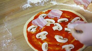 Putting mushrooms and bakon on pizza dough with tomato souce. Food footage. Hands of a chef with ingredients for pizza. video