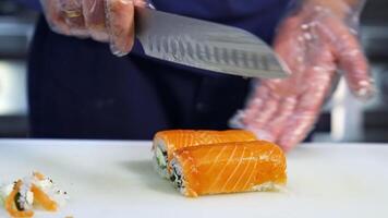 Chef cuts sushi with sharp knife into pieces. The process of sushi cooking, preparing. Japanese cuisine concept. video