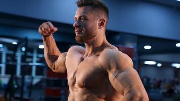 Circle view on bodybuilder without shirt in gym. Man with strong hands and big muscles. Slow motion. video